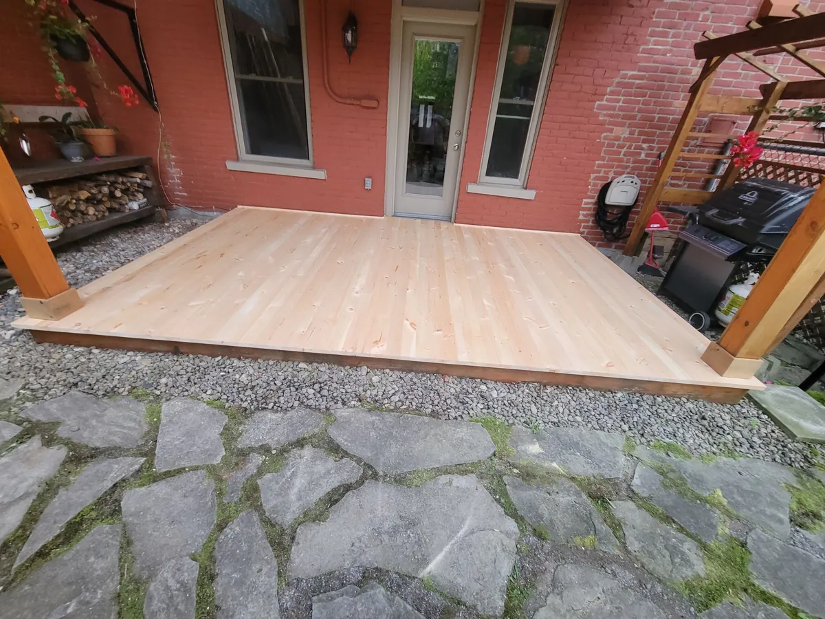 La même cour, terrasse en bois terminée devant la porte-fenêtre de la maison de brique